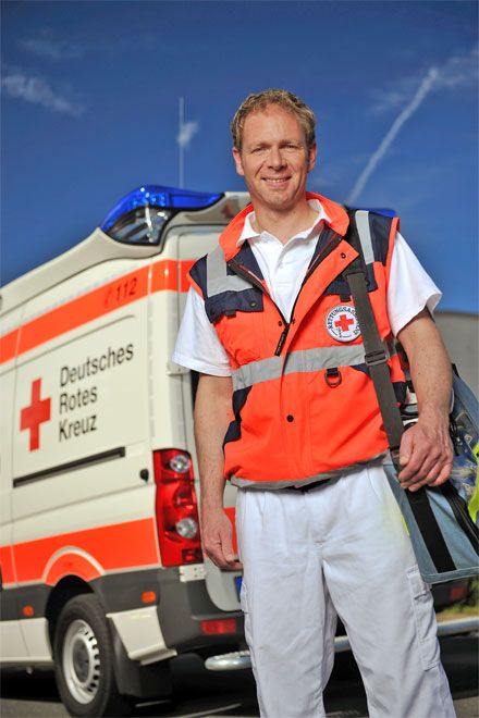 Foto: Ein DRK-Rettungssanitäter steht mit Notfallausrüstung vor einem Rettungswagen.